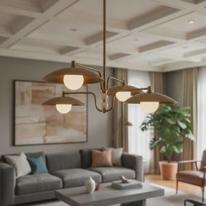 Puede incluir: Una lámpara de araña de latón con cinco luces, cada una con un globo blanco y una pantalla en forma de platillo. Cuelga en un salón con un sofá gris, obras de arte y una gran planta en maceta.