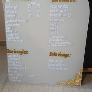 May include: An arched, frosted acrylic sign featuring gold leaf accents at the top and bottom corners. The sign displays a beauty service menu with headings for lash, smile, nail, and facial treatments, including the logo Océ Art Beauty.