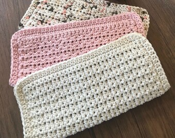 May include: Three crocheted dishcloths stacked on top of each other. The top dishcloth is beige, the middle dishcloth is pink, and the bottom dishcloth is beige with brown and pink flecks.