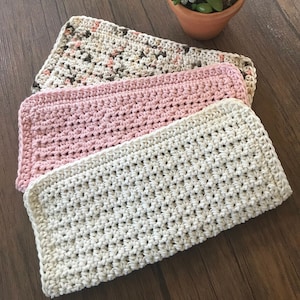 May include: Three crocheted dishcloths stacked on top of each other. The top dishcloth is beige, the middle dishcloth is pink, and the bottom dishcloth is beige with brown and pink flecks.