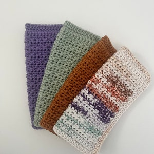 May include: Four crocheted dishcloths in different colors and patterns. The dishcloths are stacked on top of each other. The top dishcloth is white with brown and purple stripes. The next dishcloth is brown. The next dishcloth is green. The bottom dishcloth is purple.