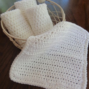 May include: A white crocheted blanket in a white wire basket with three smaller white crocheted squares.