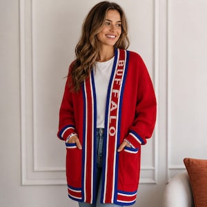 May include: A red knit cardigan featuring long sleeves, two front pockets, and a white and blue striped trim along the open front. The word BUFFALO is printed in white capital letters vertically along the left side of the front placket.