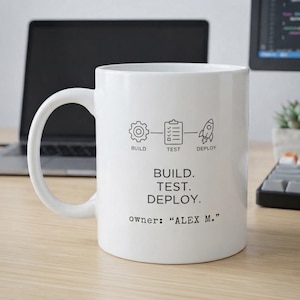May include: A white ceramic mug featuring black line art icons of a gear, a checklist, and a rocket labeled BUILD, TEST, and DEPLOY. Below the icons, the text reads BUILD. TEST. DEPLOY. and owner: "ALEX M." in a clean, sans-serif font.