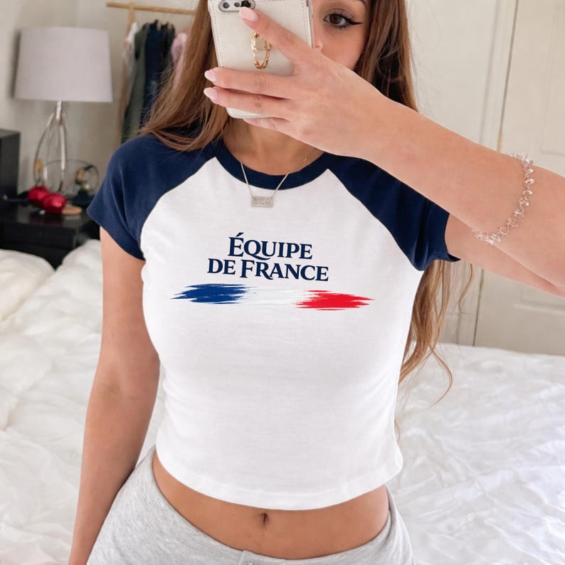 May include: White crop top with navy blue sleeves and a crew neck. The shirt displays the text "&Eacute;QUIPE DE FRANCE" and a horizontal tricolour design in blue, white, and red, representing the French flag.