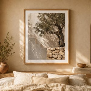Peut inclure: Une impression d'art encadrée représentant une photographie d'un olivier poussant à côté d'un mur en pierre et d'un escalier. L'image présente des tons neutres et chauds avec la lumière du soleil projetant des ombres sur le mur texturé.