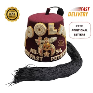 May include: A maroon fez hat featuring gold and white beaded lettering that reads POOLA, with a central emblem depicting a sword and crescent moon. The hat includes a long black tassel attached to the top and white beaded text at the base.