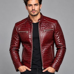 Può includere: Una giacca rosso scuro con una texture lucida in rilievo effetto pelle di coccodrillo. La giacca presenta un colletto alla coreana con chiusura a bottone automatico, una cerniera frontale argentata e due tasche pettorali con cerniera.