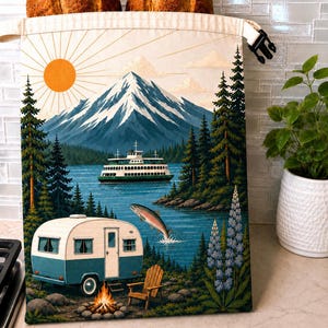May include: A cream-colored fabric bread bag with a roll-top closure and black plastic buckle. The front features a printed landscape illustration of a snow-capped mountain, a ferry on a lake, a jumping fish, a camper, a campfire, and pine trees.