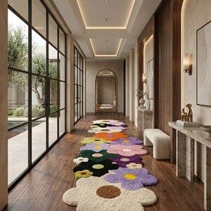 May include: A long, runner-style rug featuring a repeating pattern of large, multi-colored flower shapes. The rug is composed of plush, tufted sections in shades of cream, lavender, dark green, black, orange, and yellow, laid on a wooden floor.