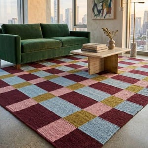 Peut inclure: Un tapis rectangulaire présentant un motif à carreaux répétitif dans des tons de bordeaux profond, rose clair, bleu sourd et vert olive. Le tapis possède une surface tissée texturée et recouvre une grande partie de l'espace au sol.