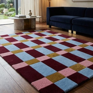 May include: A rectangular area rug featuring a repeating geometric grid pattern composed of alternating solid blocks in deep burgundy, light blue, muted pink, and olive green, with a textured pile surface covering the entire floor space.
