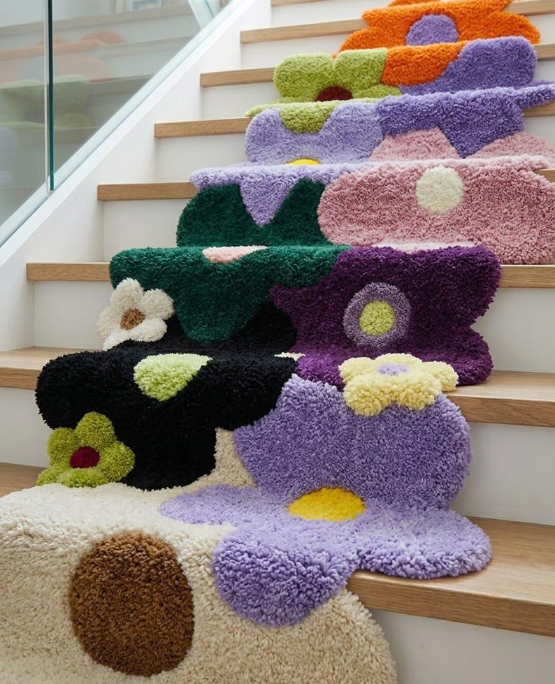 May include: A set of tufted stair treads featuring a multi-colored floral pattern. Each tread displays large, abstract flower shapes in shades of orange, lime green, purple, pink, dark green, black, yellow, cream, and brown with a textured pile.