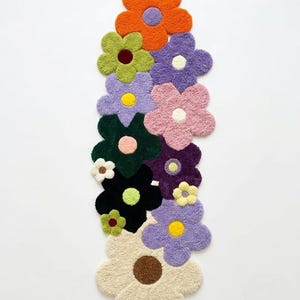 May include: A tufted rug shaped like a vertical cluster of overlapping flowers in various colors including orange, lime green, lavender, pink, dark green, black, cream, and purple, each featuring a contrasting circular center in a different hue.