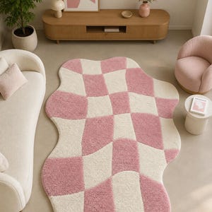 Könnte beinhalten: Ein rosa-weiß karierter Teppich mit einer wellenförmigen Form. Der Teppich liegt auf einem hellen Boden, umgeben von Möbeln in neutralen Farben, darunter ein Sofa, ein Sessel und ein Holzschrank. Der Raum ist in einem modernen, minimalistischen Stil eingerichtet.