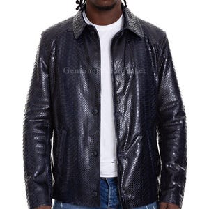 May include: A dark navy blue jacket featuring a textured snakeskin pattern, a classic collar, and a front button closure. The garment is worn over a plain white t-shirt and blue denim jeans, showcasing a structured fit with long sleeves.