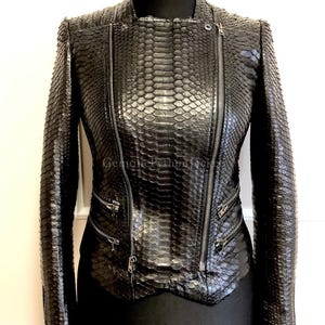 May include: A black jacket featuring a textured snakeskin pattern throughout. The garment includes a full-length off-centre front zip, two zipped pockets on the lower front, and long sleeves with zipped cuffs, all finished with silver-tone hardware.