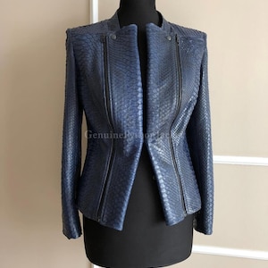 Könnte beinhalten: Eine blaue Jacke mit strukturiertem Schlangenledermuster und Stehkragen. Das Kleidungsstück verfügt über zwei vertikale schwarze Reißverschlüsse auf der Vorderseite, lange Ärmel und eine strukturierte Passform. Der Text Genuine Python ist sichtbar.