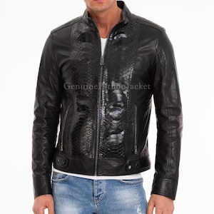 May include: A black jacket featuring a central panel with a textured snakeskin pattern, a stand-up collar, and a full-length front zip. The garment includes two zipped side pockets and a horizontal band at the hem with metallic snap details.