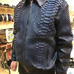 Könnte beinhalten: Eine dunkelblaue Jacke mit einer strukturierten Schlangenhaut-Optik auf der Vorderseite und den Ärmeln. Das Kleidungsstück verfügt über einen klassischen Kragen, einen zentralen Metallreißverschluss und glatte lederartige Seitenteile. Der Text GenuinePythonJacket ist sichtbar.