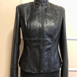 May include: A black jacket with a textured snakeskin pattern and a full-length front zip fastening. The garment features a high collar and long sleeves, with the text GenuinePythonJacket visible on the front surface of the material.