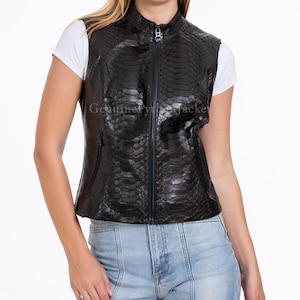 May include: A black sleeveless waistcoat featuring a textured snakeskin pattern, a high collar, and a full-length front zip fastening. The garment includes two side pockets with zip fastenings and is worn over a plain white short-sleeved t-shirt.