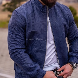 May include: A dark blue jacket with a textured snakeskin pattern, featuring a stand-up collar, a full-length silver zip, and ribbed cuffs. The text "GenuinePythonJacket" is visible on the front of the garment, which is worn over a white shirt.