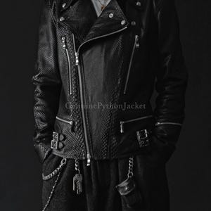 Peut inclure: Une veste de moto noire avec un motif texturé en peau de serpent, dotée de fermetures éclair en métal argenté, de boutons-pression sur les revers et de boucles latérales réglables. Le texte GenuinePythonJacket est imprimé sur le devant.