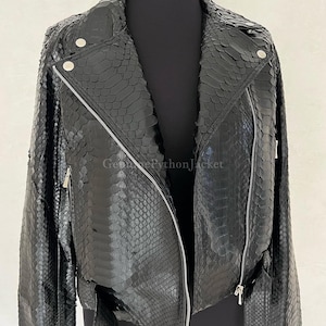 May include: A black motorcycle jacket crafted from textured python skin featuring a notched lapel, silver-toned metal zips, and a buckled belt at the hem. The jacket displays a distinct scale pattern and includes the text GenuinePythonJacket.