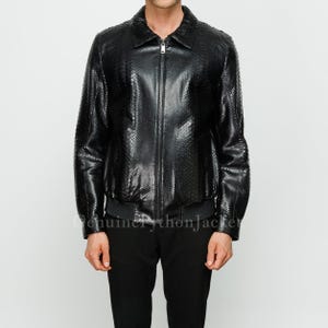 May include: A black jacket with a textured snakeskin pattern, featuring a classic collar, a full-length front zip fastening, and ribbed cuffs at the hem. The garment has long sleeves and a structured fit, showcasing a glossy finish throughout.