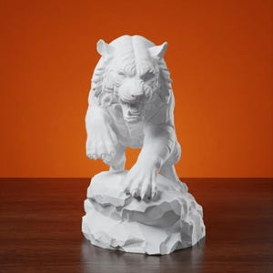 Könnte beinhalten: Eine mattweiße Skulptur eines Tigers in Sprungposition mit geöffnetem Maul, das die Zähne zeigt. Der Tiger thront auf einem zerklüfteten, felsartigen Sockel. Die Figur weist detaillierte Fellstrukturen und eine ausgeprägte Muskulatur auf.