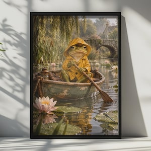 May include: A framed wall art print depicting a green frog wearing a yellow hooded raincoat, sitting in a small wooden rowboat on a calm pond. The scene includes a wooden oar, pink water lilies, lily pads, and a stone bridge in the background.