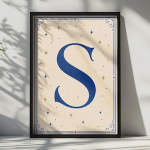 以下が含まれることがあります： クリーム色の背景の中央に、大きく太いダークブルーの文字「S」が配置された額装済みのウォールアートプリント。デザインは、装飾的なコーナーが付いた細い青い枠で囲まれており、小さな金と青の星のアイコンが散りばめられています。