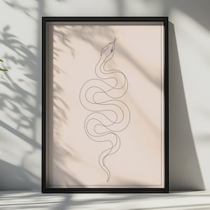 May include: A framed wall art print featuring a single continuous black line drawing of a snake on a solid light beige background. The snake is depicted in a vertical, winding position with its head at the top, enclosed in a thin black frame.