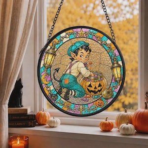Può includere: Un acchiappasole circolare in vetro colorato raffigurante un giovane diavoletto con corna e coda, che indossa un berretto e una salopette blu, mentre infila la mano in una zucca di Halloween piena di caramelle, con due lanterne e una catena.