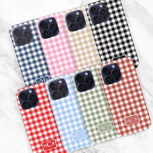 May include: Eight smartphone cases featuring a gingham check pattern in various colors including navy, pink, beige, black, red, light blue, sage green, and terracotta. Each case has a rectangular monogram label with white text at the bottom.