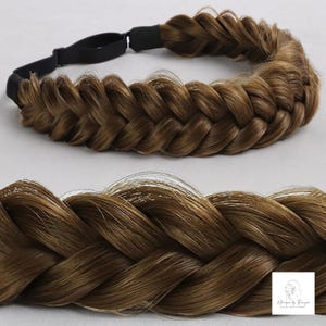 May include: A brown braided hair headband featuring a thick, fishtail-style synthetic hair braid attached to a black elastic band. The hair has natural-looking highlights and a smooth texture. A small white logo square is visible in the corner.