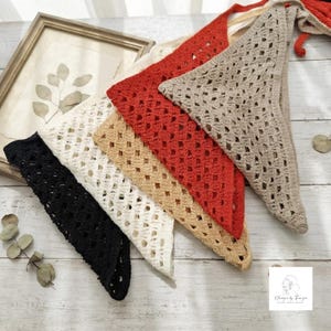 May include: A collection of four triangular crochet bandanas in black, white, tan, and rust orange. Each piece features an openwork diamond pattern and is crafted with a textured yarn. The items are arranged in a layered, overlapping fan formation.