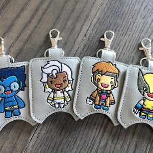 May include: Four gray hand sanitizer holders with silver keychains. Each holder features an embroidered cartoon character from the X-Men: Beast, Storm, Gambit, and Wolverine.