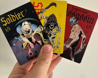 May include: Three rectangular trading cards with illustrated characters. The black card features a soldier by a fire, the yellow card shows a skeleton with a scythe, and the red card depicts an assassin with a blade and a skull mask.