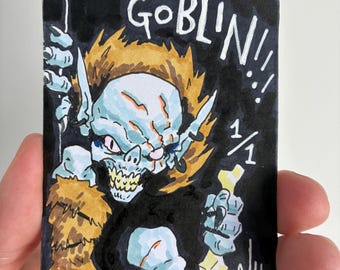 May include: A rectangular trading card featuring a hand-drawn illustration of a blue-skinned goblin with spiky orange hair, sharp teeth, and fur-trimmed clothing. The card has a black background, the text GOBLIN!!!, the fraction 1/1, and the signature A/H 2/6.