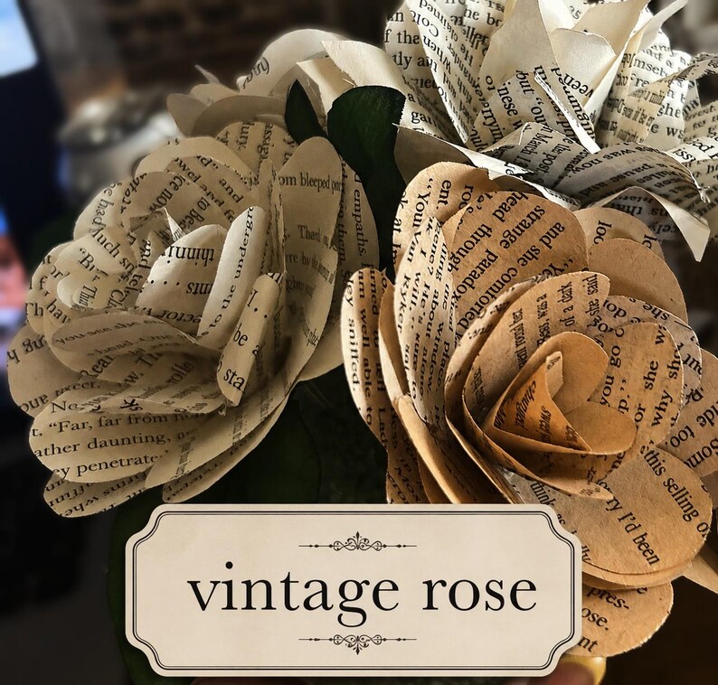 May include: A bouquet of paper flowers crafted from vintage book pages with visible printed text. The flowers feature layered petals in shades of cream and tan. A rectangular label with a decorative border displays the text vintage rose.