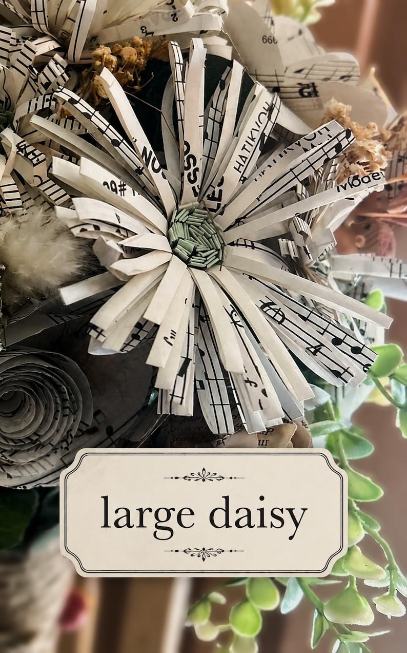 May include: A handcrafted daisy flower made from strips of white paper printed with black musical notation. The center of the flower features small, light green cylindrical elements. A rectangular label below reads large daisy.