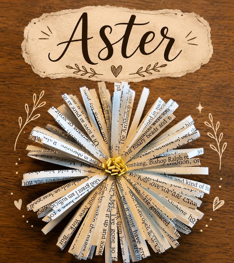 May include: A decorative paper flower crafted from strips of printed book pages with black text, featuring a small yellow center. Above the flower, a beige label with a torn-edge design displays the word Aster in black script with a small heart.