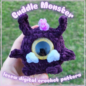 May include: A handmade purple crochet monster with large, reflective eyes and small white and pink accents. The text "Cuddle Monster" and "losew digital crochet pattern" are displayed on the image.