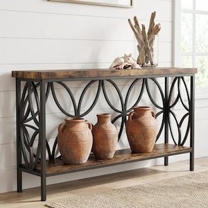 May include: A rectangular console table with a dark wood grain top and bottom shelf, supported by a black metal frame featuring large circular geometric patterns. Three terracotta-colored ceramic vases sit on the bottom shelf.
