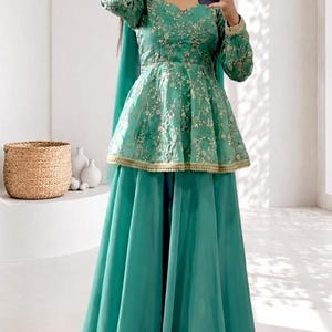 Peut inclure: Ensemble vert teal composé d'un haut à manches longues avec broderie dorée et taille péplum, associé à une jupe longue assortie. La tenue comprend une écharpe assortie. Idéale pour les occasions spéciales.