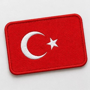 May include: A rectangular embroidered patch featuring a vibrant red background with a white crescent moon and a five-pointed star centered on the surface. The patch has rounded corners and a thick, stitched red border around the entire perimeter.
