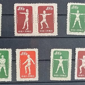 以下が含まれることがあります： 様々な運動のポーズをとる様式化された人物が描かれた、ヴィンテージ切手のコレクションです。切手は赤、緑、青で、「400」の額面と中国語のテキストが記されています。切手は長方形で、暗い面に配置されています。