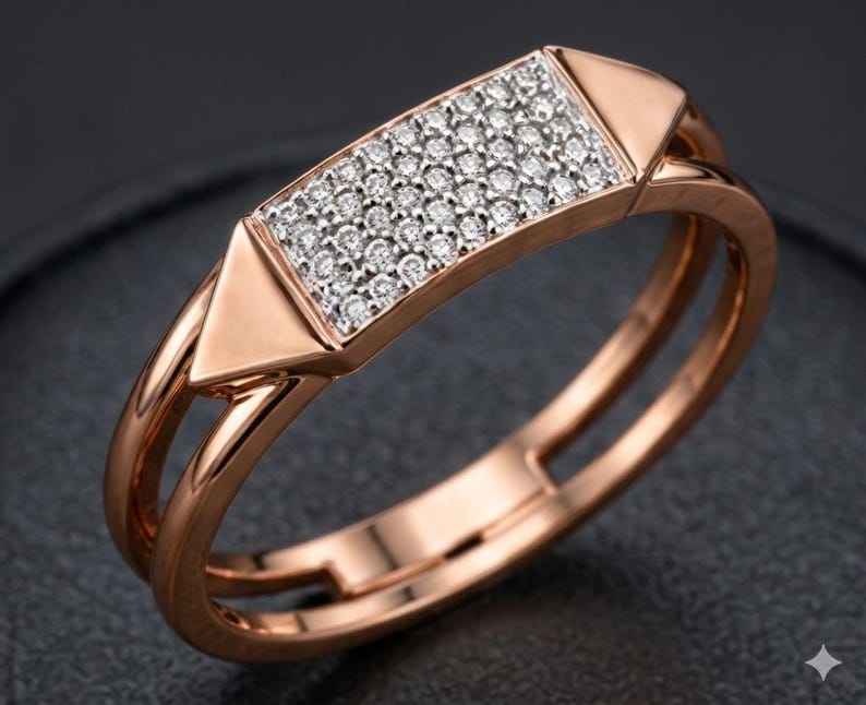May include: Rose gold ring with a rectangular center encrusted with small, sparkling diamonds. The ring features a geometric design with a double band and triangular accents on each side of the diamond-studded rectangle. The ring is set against a dark background.
